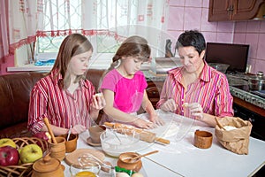 Mom teaching her two daughters cooking on the kitchen.