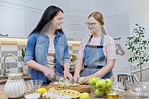 Mom and teen daughter cooking apple pie together at home kitchen