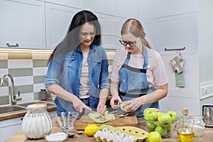 Mom and teen daughter cooking apple pie together at home kitchen