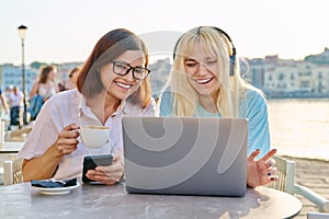 Mom and teenage daughter looking at laptop together, sitting in an outdoor cafe