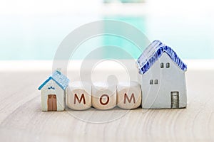 Mom text on wooden cube with miniature house over blurred background