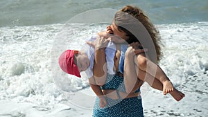 Mom tickles her little son, sea on background.