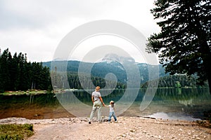 Mom and toddler daughter stand and look at Black Lake, Durmitor. Travel with kids. Family vacation.