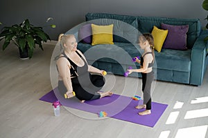 Mom together with child is engaged in sports fitness with dumbbells. Joint family training at home