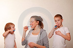 Mom and two blond boys brush their teeth