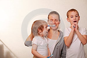 Mom and two blond boys brush their teeth