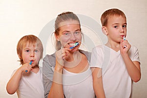 Mom and two blond boys brush their teeth