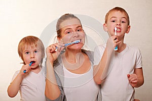 Mom and two blond boys brush their teeth