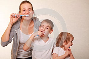 Mom and two blond boys brush their teeth