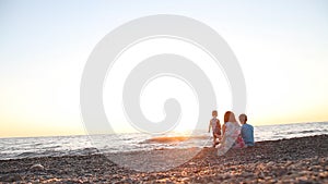 Mom with two boys, sons of rest on the beach by the sea at sunset,