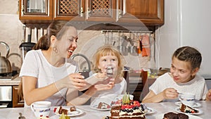 Mom and two daughters are having a tea with homemade chocolate cake in the kitchen, family birthday at home.