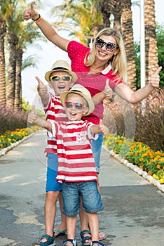 Mom and two son in sunglasses and hats to walk through the alley of palm trees.Family summer vacation.