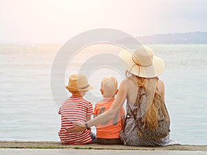 Mom and two sons sit on the pier and admire the sea and the moun