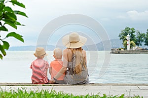 Mom and two sons sit on the pier and admire the sea and the mountains in the distance. Back view