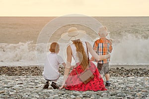 Mom and two sons sitting on the beach and watching the waves. View from the back