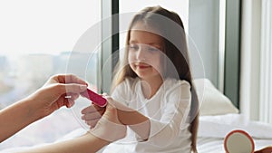 Mom uses a file to clean her cute daughter's nails before applying a manicure.