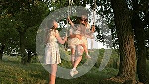 Mom walks with children and swings on a swing in the park. The concept of a happy family. dream of flying. The concept