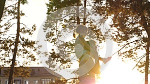 Mom walks with her daughter on her shoulders under the trees. mother carries on her shoulders her beloved child, in park