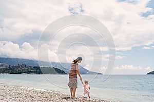 Mom walks with a little girl holding her hand along the pebble beach