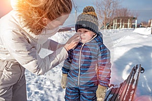 Mom wipes her nose with a napkin, her little boy`s boy is 4 years old. In winter, on the nature, the background of the