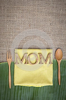 Mom wooden text on yellow napkin on hessian and green banana leaf background