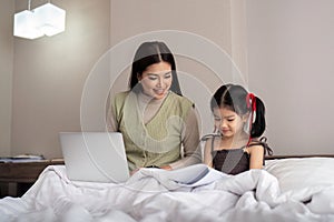 Mom work from home with children. Mother working on bed laptop in bedroom with child daughter. Funny authentic lifestyle