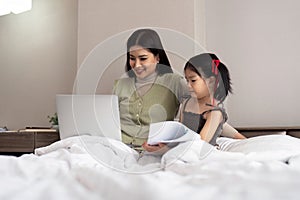 Mom work from home with children. Mother working on bed laptop in bedroom with child daughter. Funny authentic lifestyle
