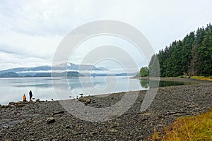 A mom and young daughter enjoying the beautiful view of the calm ocean and forest during the rain at Kagan Bay, Haida Gwaii