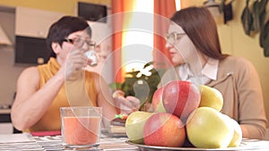 Mom and young daughter with glasses drink tea or coffee in the kitchen and eat cakes, talk, laugh. In the foreground