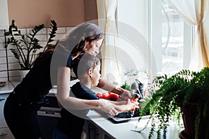 Mom and young son wash fresh vegetables in the kitchen