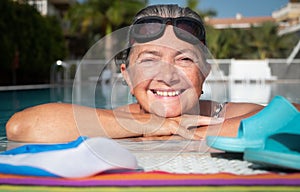 A moment of breath for the attractive senior woman who loves to swim. Large smile. Outdoor pool with blue water. Healthy activity