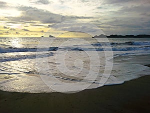 The moment before the golden hours the waves foam towards the beach sand.