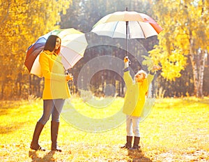 Moment of happiness! Happy family with umbrellas in sunny autumn rainy day, young mother and child in jacket outdoors