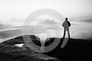 Moment of loneliness. Man on the rock empires and watch over the misty and foggy morning valley to Sun