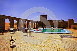 Moment of relaxation in a hotel swimming pool amids moroccan desert, with sand dunes on the horizon.