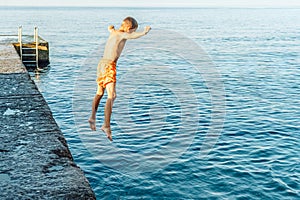 Moment of schoolboy jumping from pier into sea doing tricks