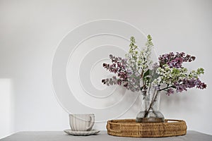 Moment of tranquility with cup of coffee, wicker tray. Floral bouquet of blooming purple and white lilacs branches in