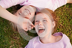 Moments with my sister. Two little girl lying happily on the grass and laughing.