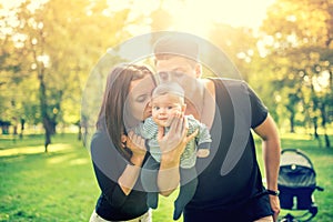 Mommy and daddy holding baby, 3 months old newborn and kissing him. Happy family with father, mother and infant. Vintage effect