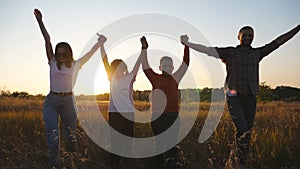 Mommy and daddy with two little children walk through grass field with raising hands at sunset. Happy parents with small
