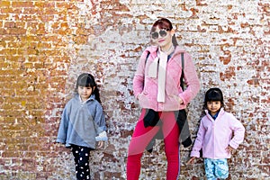 Mommy and her identical twins happy pose with old brick wall background