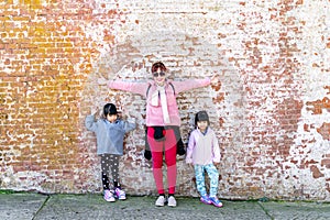 Mommy and her identical twins happy pose with old brick wall background