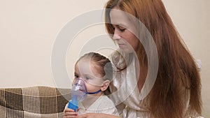 Mommy inhales a little girl in a mask with a nebulizer at home. The child is receiving respiratory therapy with a