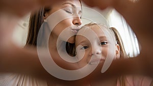 Mommy kissing small preschool smiling daughter, making love sign.