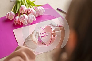 moms day. I love you, Mom. Childrens hands holding a heart card.Pink heart card and pink tulips.child makes a card for