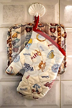 Moms kitchen - a potholder and an oven mitt hang from a plastic shell-shaped hanger on tile in a homey kitchen - closeup