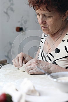 Momâ€™s hands, making dough from flour and eggs, prepare dumplings with cherries on a wooden table, this food is usually prepared