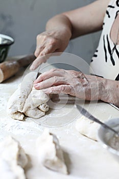 Momâ€™s hands, making dough from flour and eggs, prepare dumplings with cherries on a wooden table, this food is usually prepared