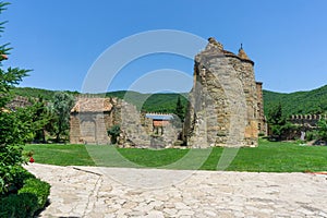 Monastery courtyard. Ruins of old church on the green grass. Part of stone wall and stone path. Daylight, blue sky