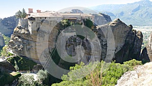 Monastery perched high up on the rocks in Meteora, Greece with mountain view beyond